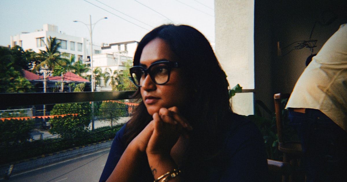 Young Indian professional sitting by a window looking pensive, representing marriage anxiety and the stress of partner search