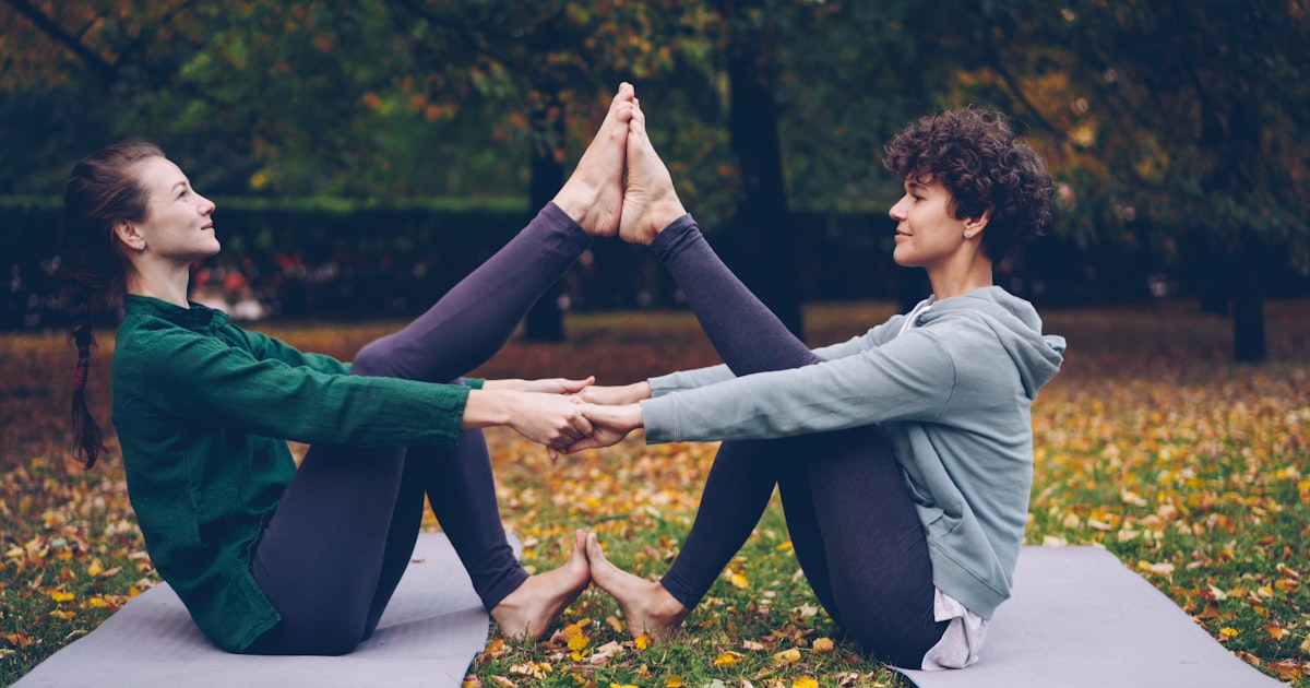 Two women doing partner yoga outdoors