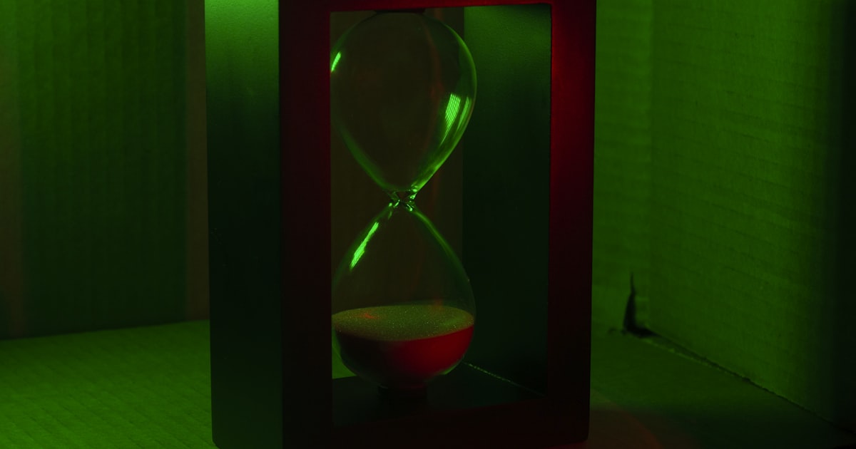 An hourglass sits in a frame under green light.