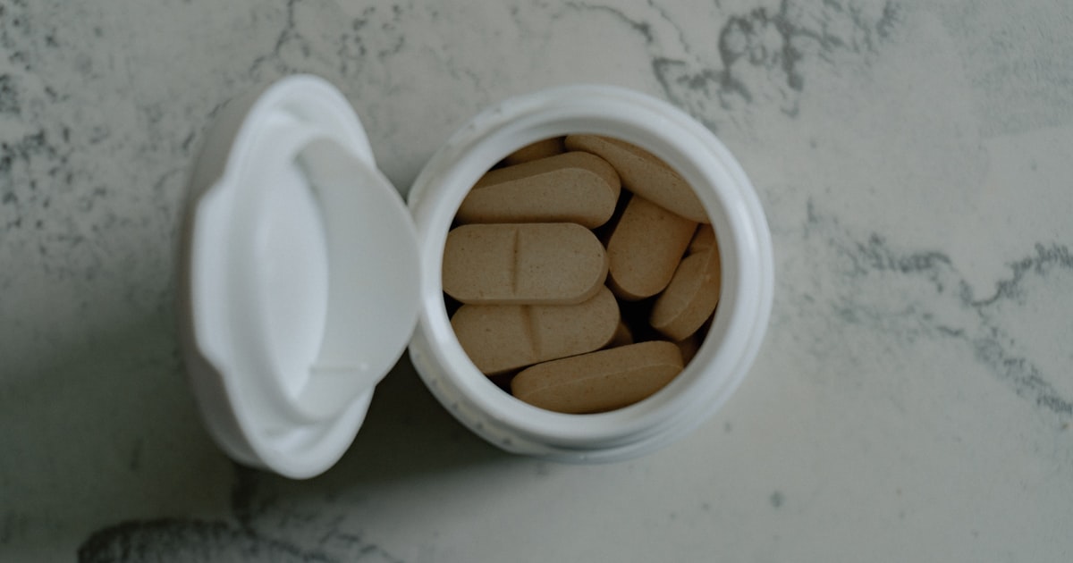 Opened bottle of beige pills on marbled surface