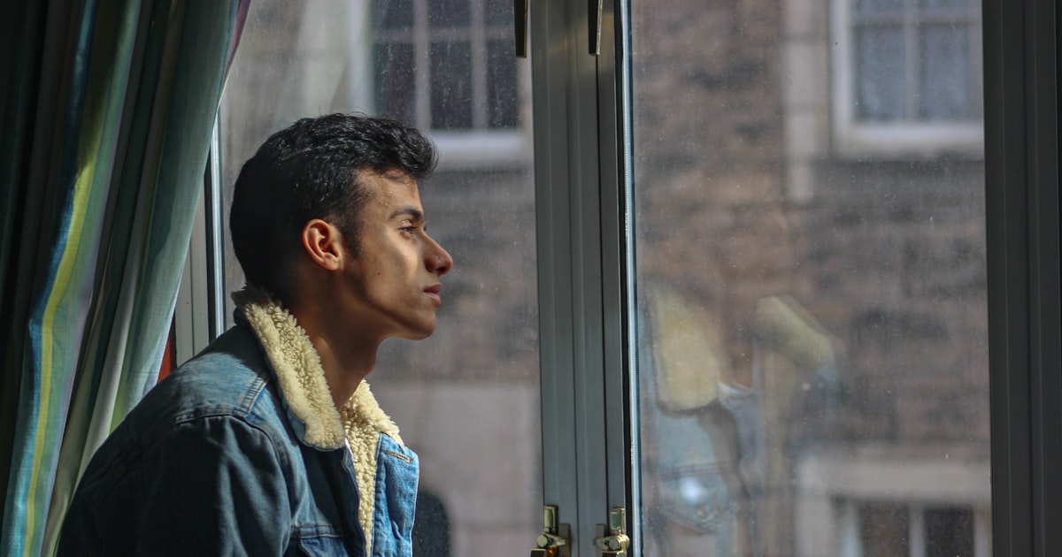 Young Indian man sitting by a window looking thoughtful with warm lighting