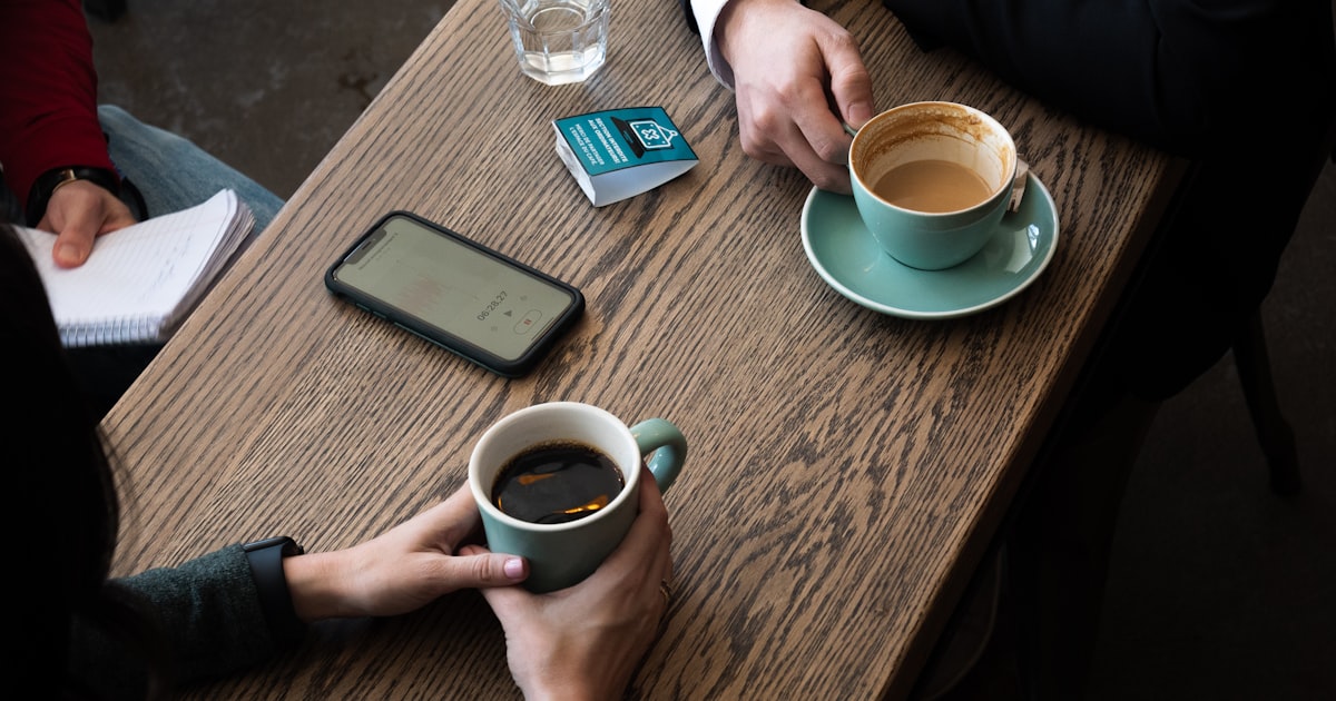 Two men meeting at a well-lit cafe exchanging a warm handshake with coffee cups on the table